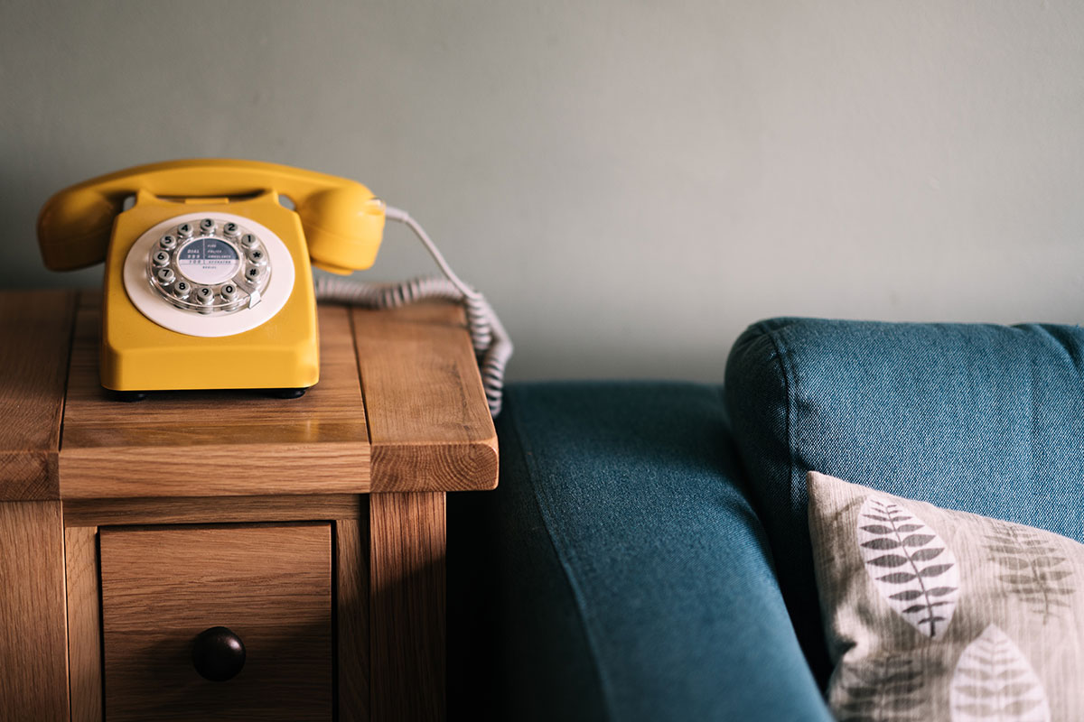 A yellow rotary phone sits on a wooden table beside a blue couch