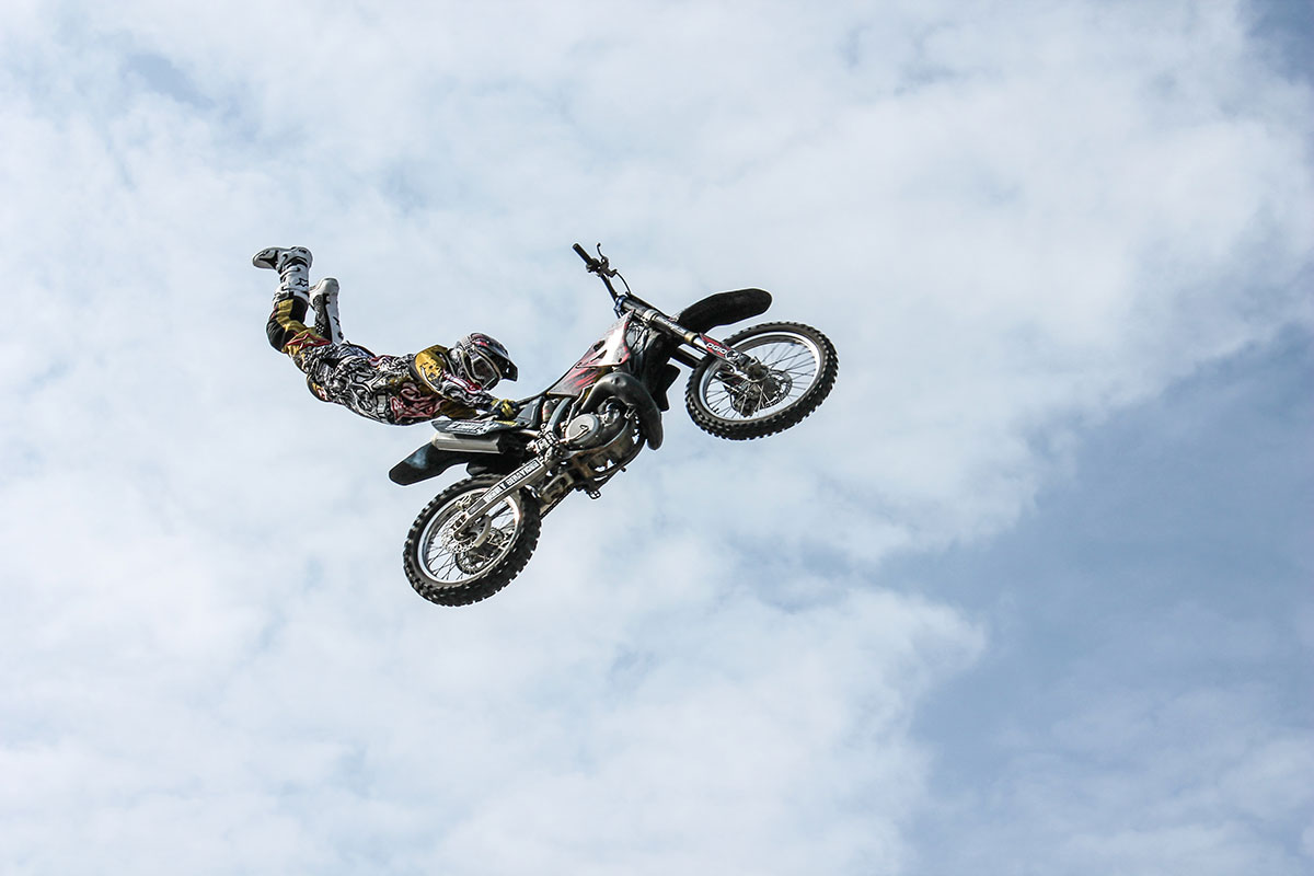 A motocross rider hangs off the back of a dirt bike suspended against the sky